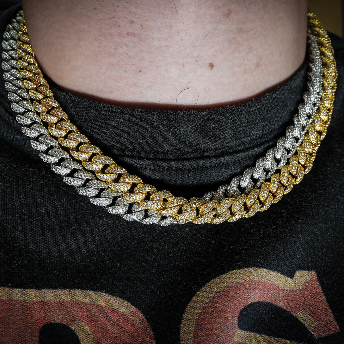 a gold and silver chain cuban link necklaces on a person wearing a black shirt with red text.