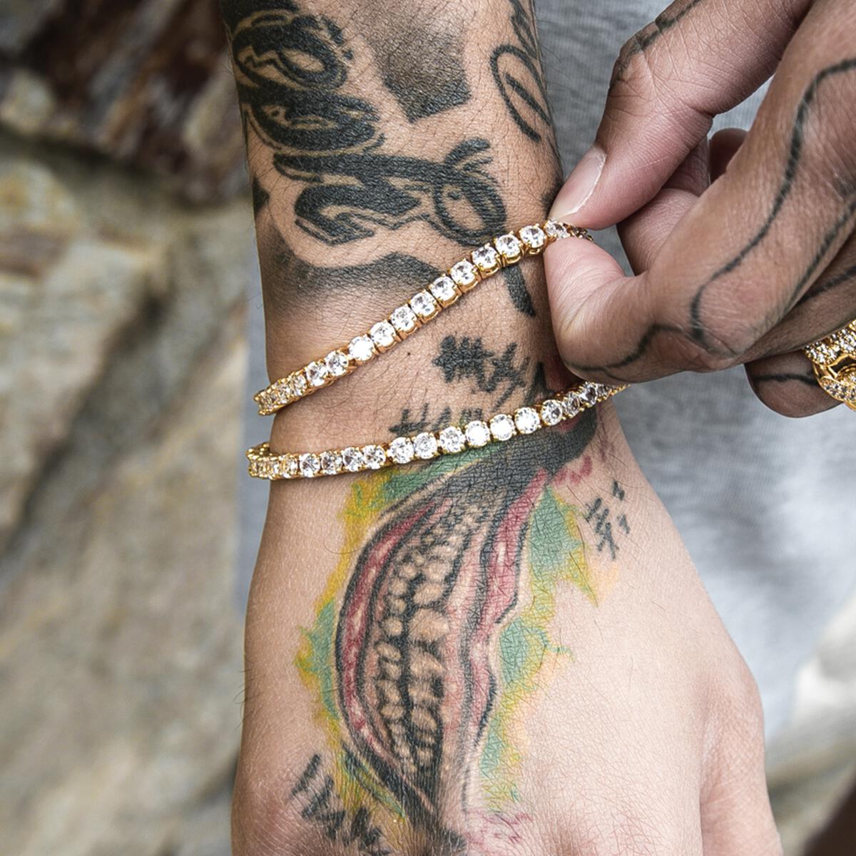 Person wearing two gold tennis bracelets on a wrist with tattoos