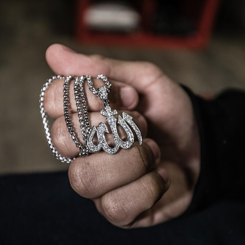 Hand holding two silver necklaces with an intricate design of Arabic calligraphy stating Allah for the pendant