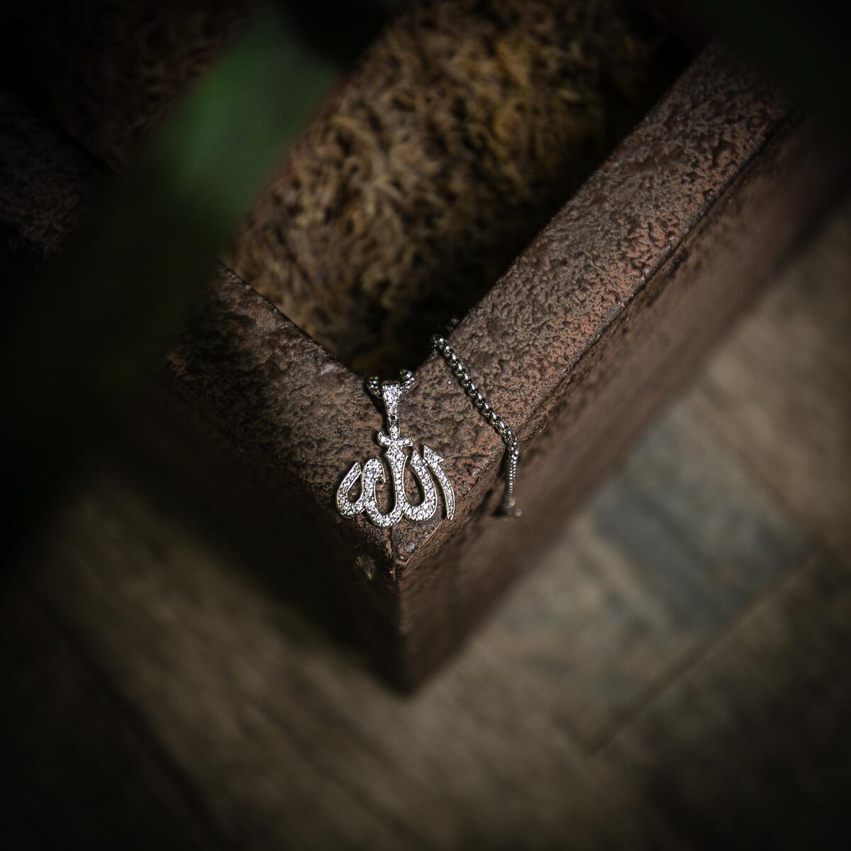 Silver necklace with an Allah pendant on a textured surface