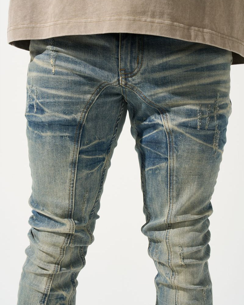 Blue distressed jeans worn with a beige oversized shirt on a white background