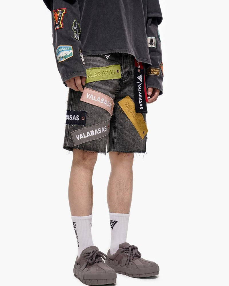 Person wearing a black jacket and gray shorts with various patches on a white background