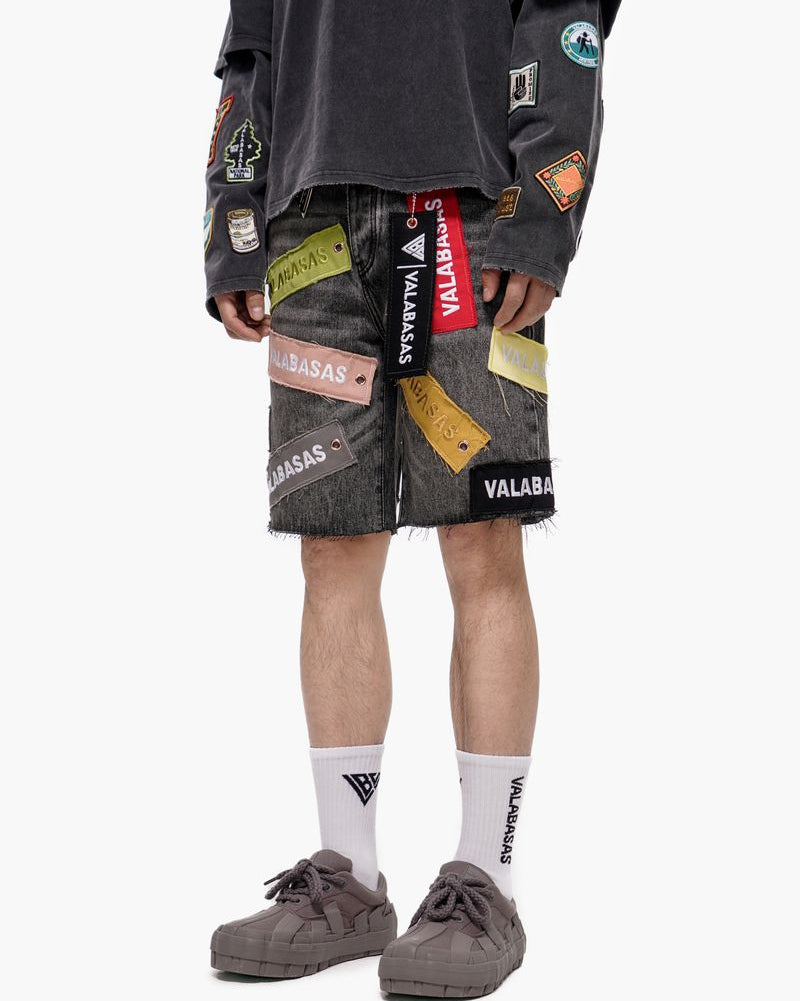 Person wearing gray shorts with colorful patches and a dark long-sleeve shirt on a white background