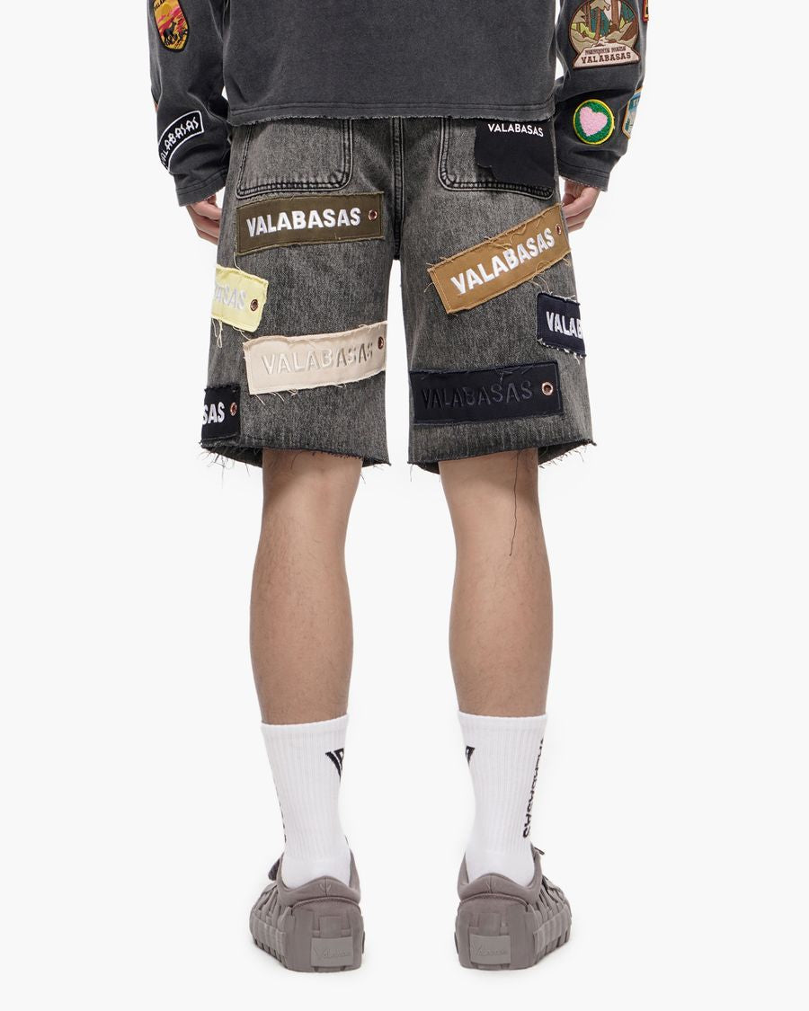 Person wearing gray shorts with patches and a dark shirt on a white background