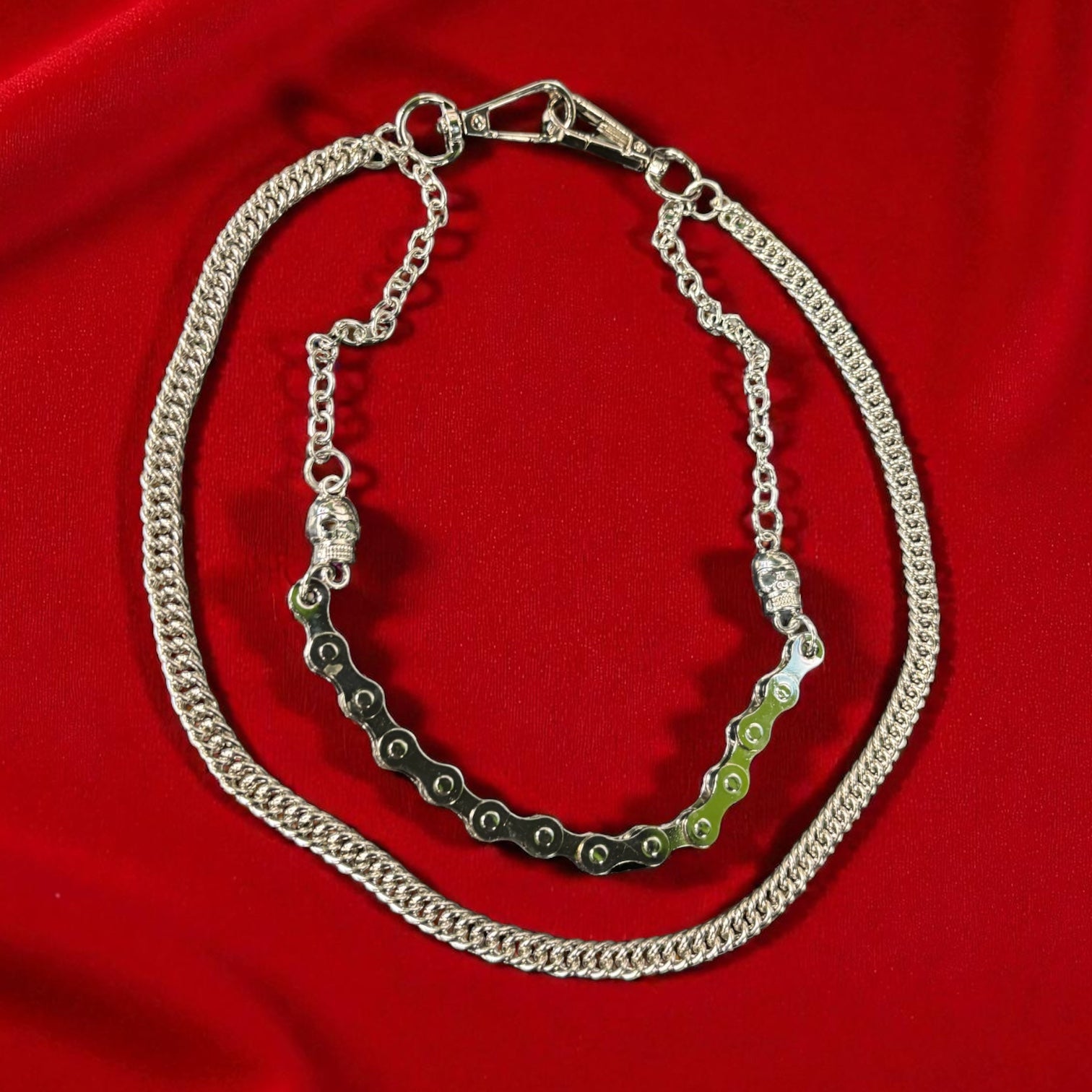 Silver chain necklace with a green bicycle chain on a red fabric background