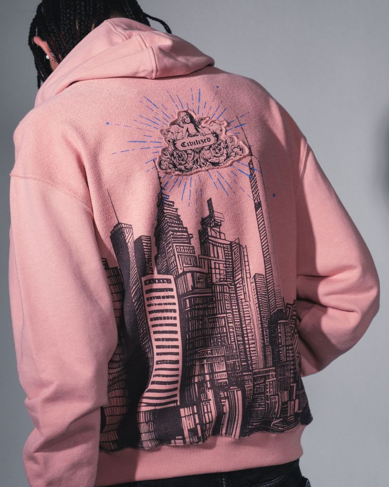 Person wearing a pink hoodie with a cityscape design on the back against a gray background