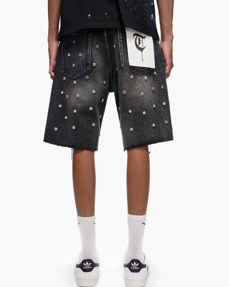 Person wearing black denim shorts with colorful studs on a white background