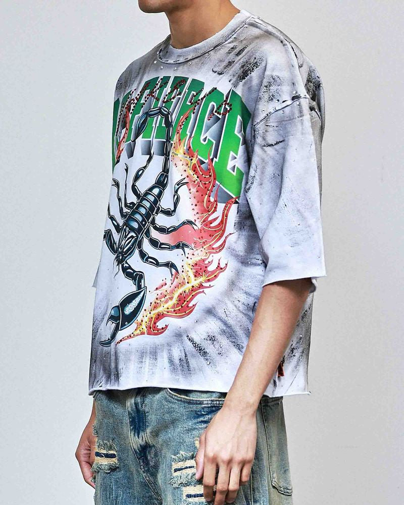 Person wearing a tie-dye t-shirt with graphic design and ripped jeans on a plain background