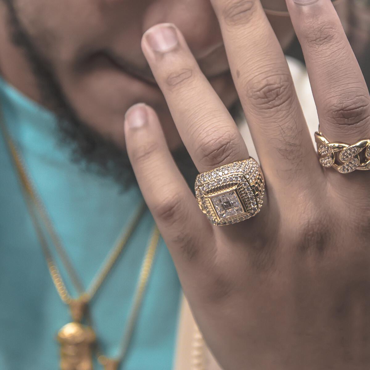 Close-up of a hand wearing the gold championship ring with diamonds, with a blurred background.