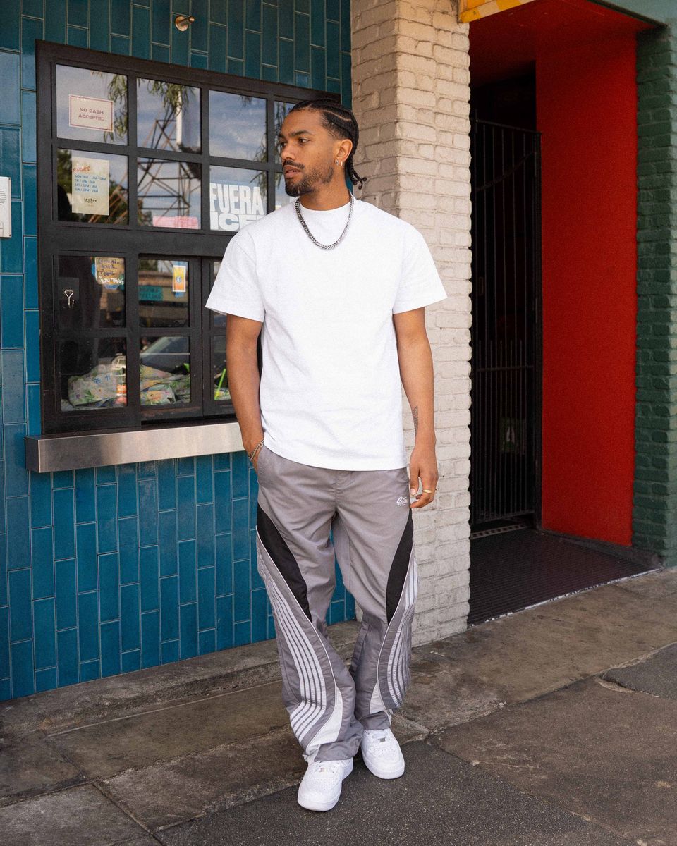 Man wearing a white t-shirt and gray pants standing in front of a colorful building.