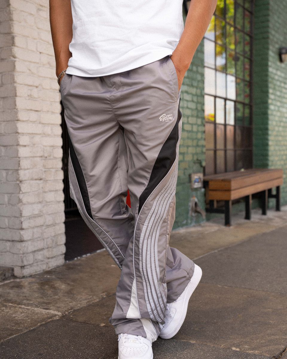 Person wearing gray pants with a brand logo, standing on a sidewalk.