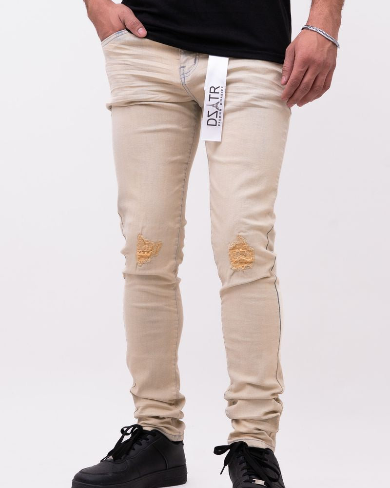 Beige distressed jeans with a brand label worn by a person on a white background