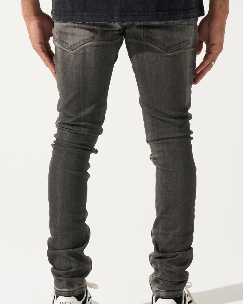 Person wearing dark gray jeans and black and white sneakers on a white background