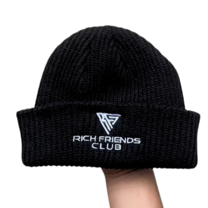 Black beanie with 'Rich Friends Club' text held by a hand on a white background