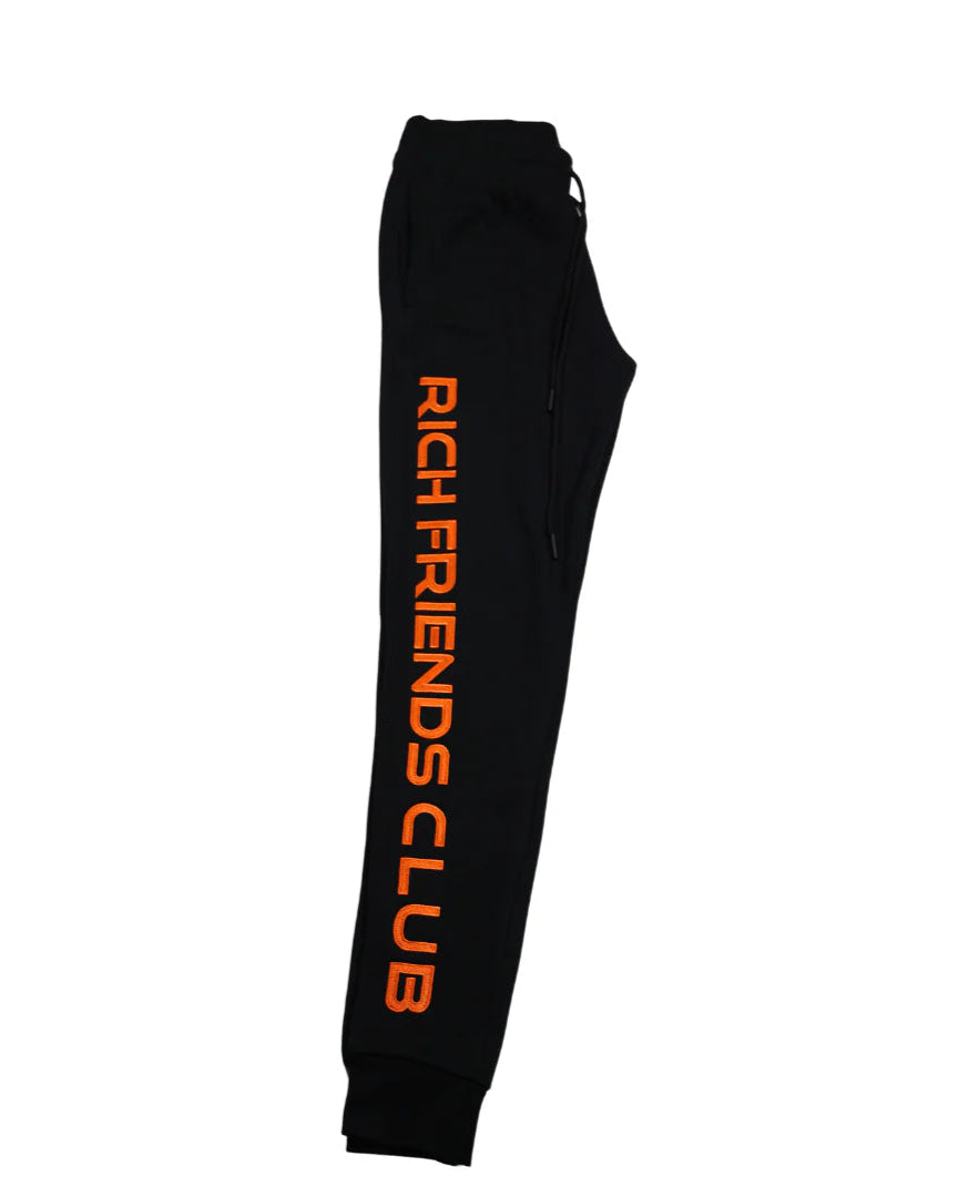 Black sweatpants with 'Rich Friends Club' text in orange on a white background