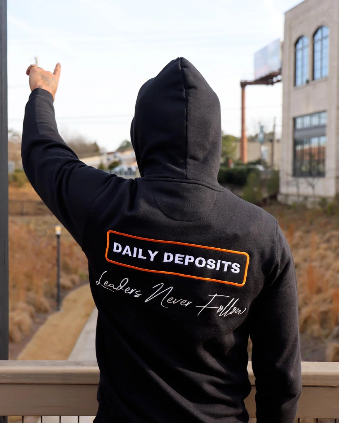 Person wearing a black hoodie with 'Daily Deposits' text, standing outdoors.