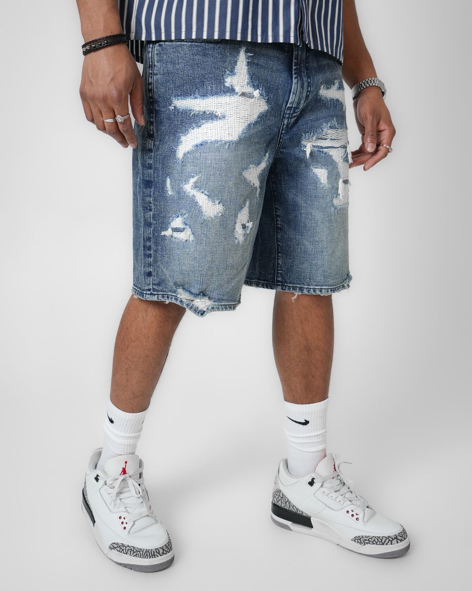 Person wearing distressed blue denim shorts with a white background