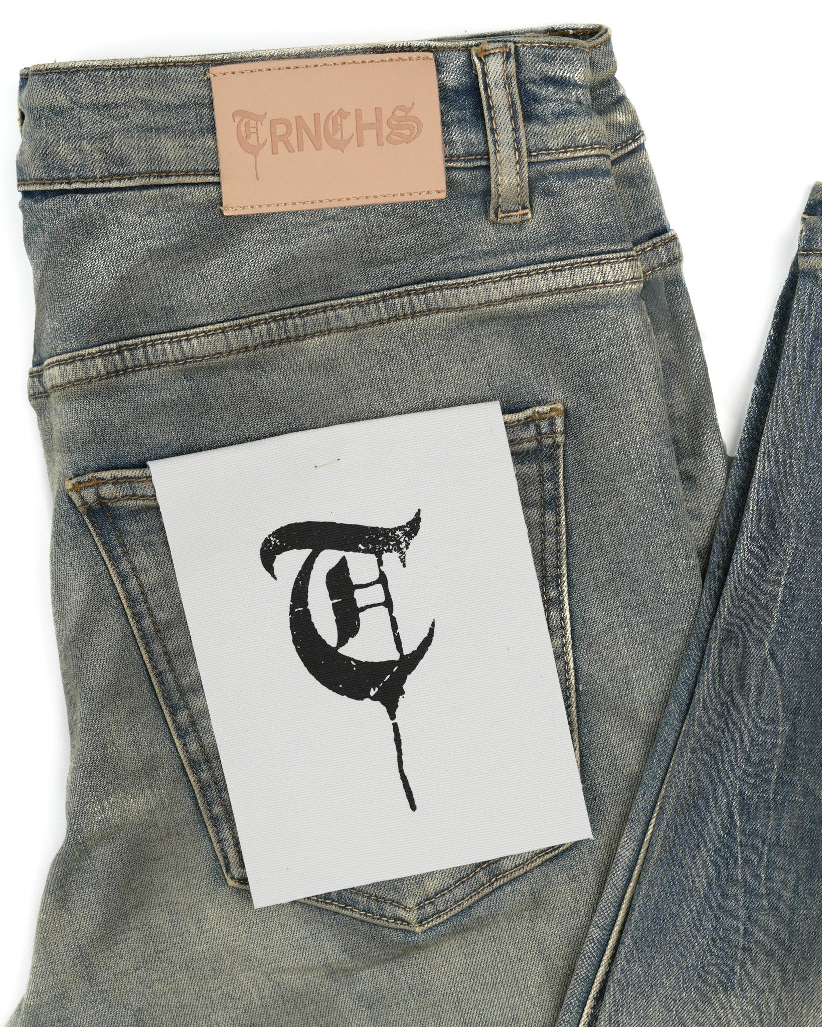 Denim jeans with a brand label and a black letter 'Q' on a white card.