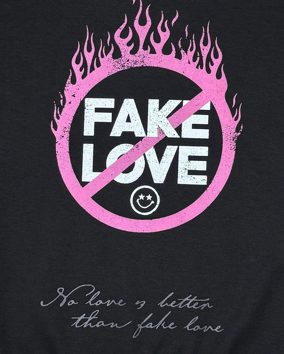Black t-shirt with 'Fake Love' design featuring pink flames and a crossed-out circle, with text below.