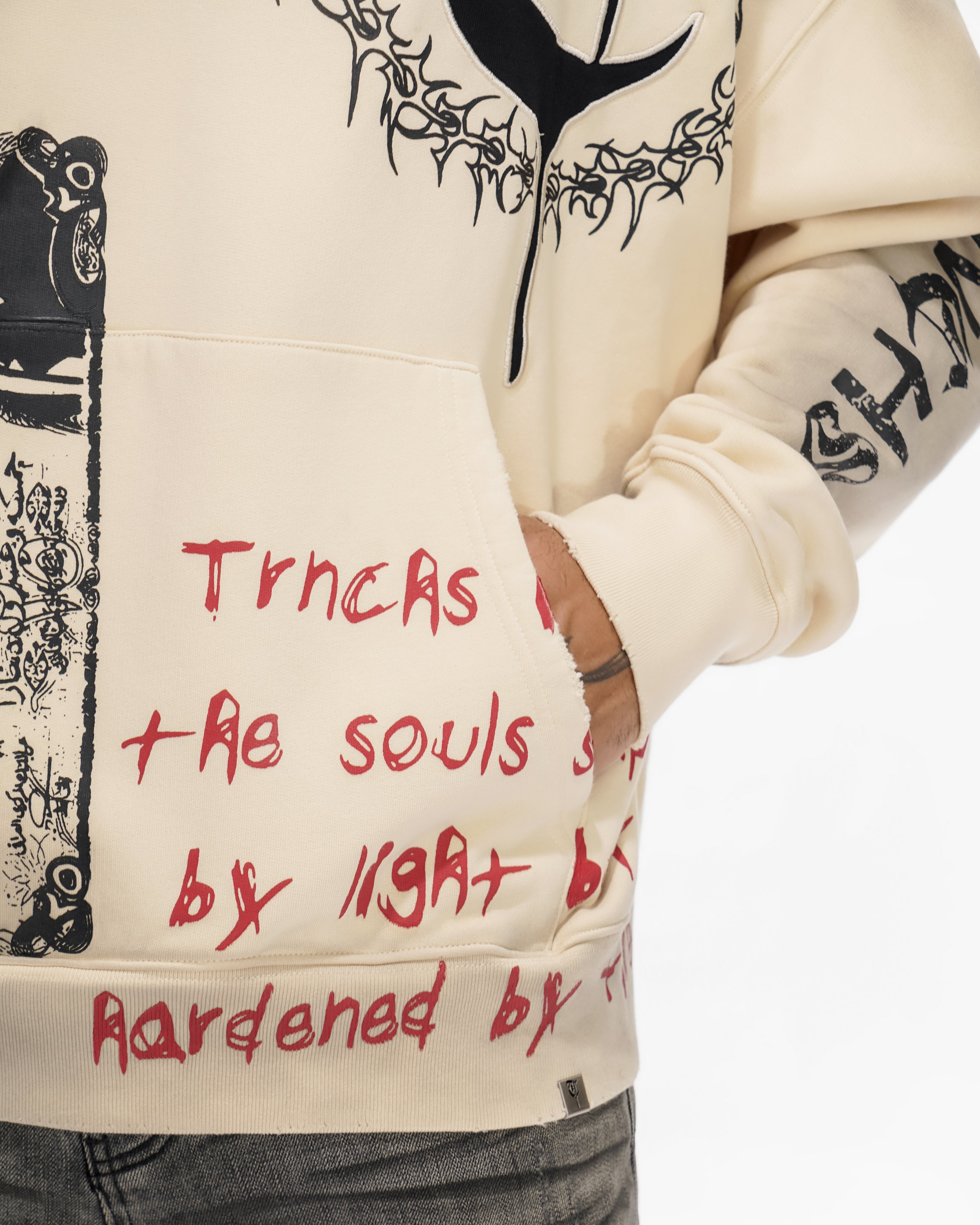 Beige hoodie with black and red text, worn by a person.