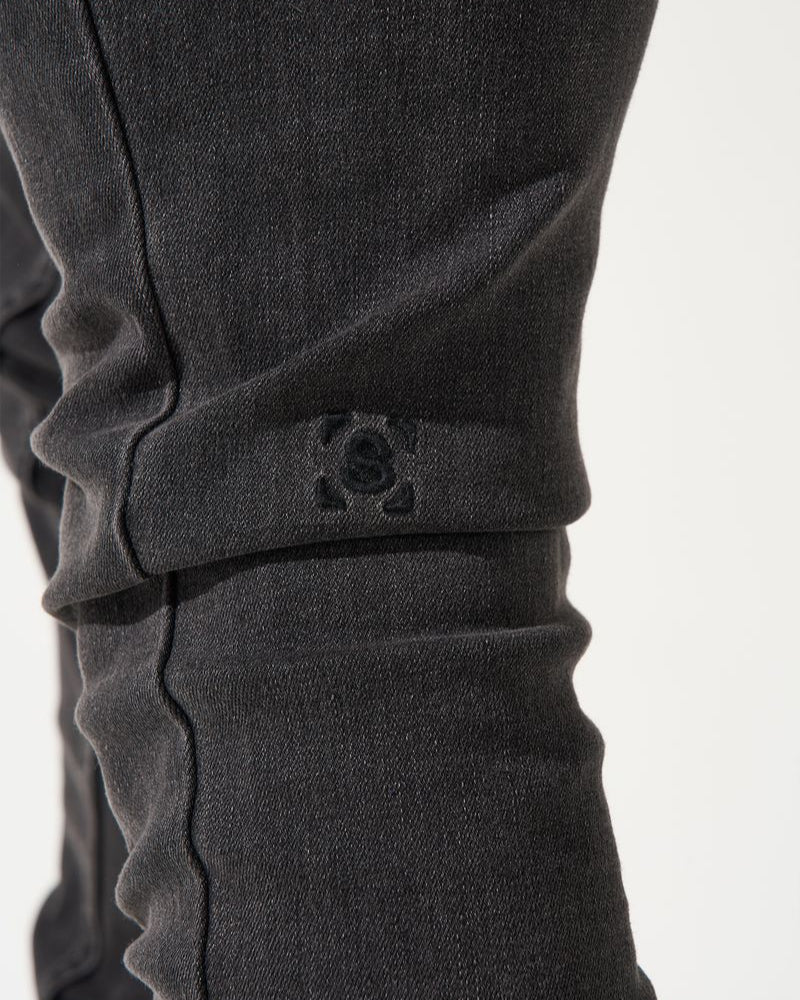 Close-up of dark gray pants with a brand logo on a white background
