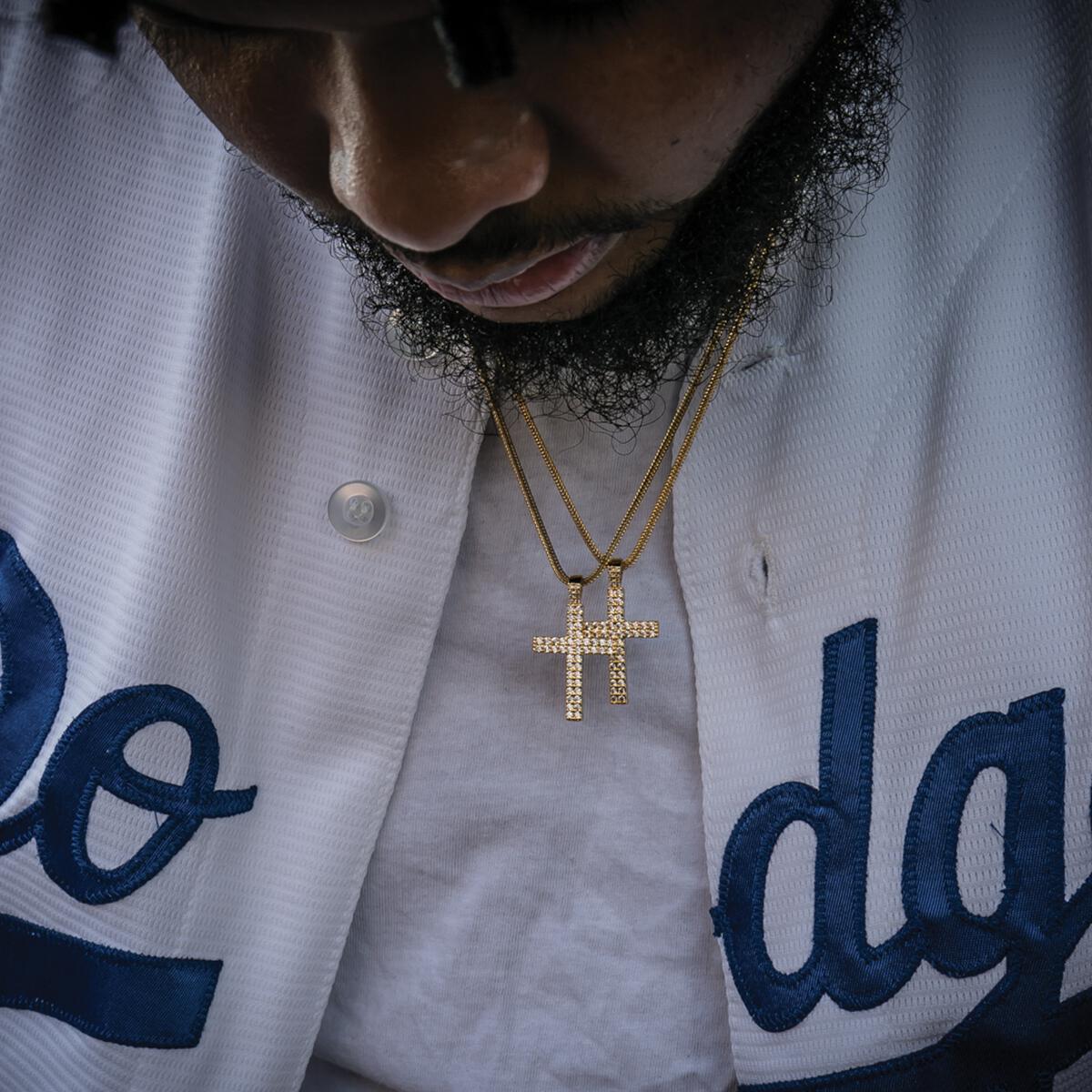 Person wearing a white jacket with blue lettering and 2 gold cross necklaces