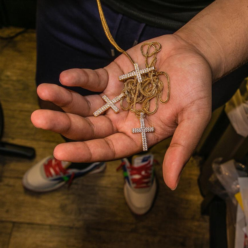 Hand holding gold cross necklaces above a wooden floor.