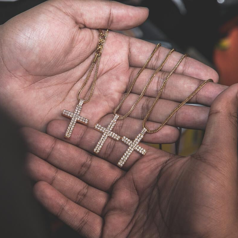 Three gold cross necklaces with diamonds held in a hand.