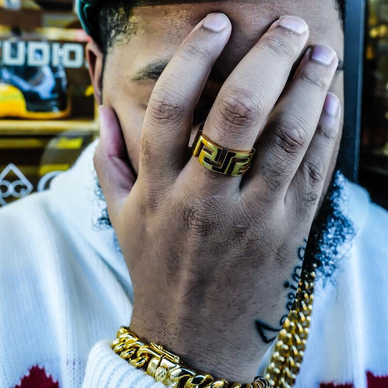 Close-up of a person wearing the greek key ring in gold, with a blurred background.