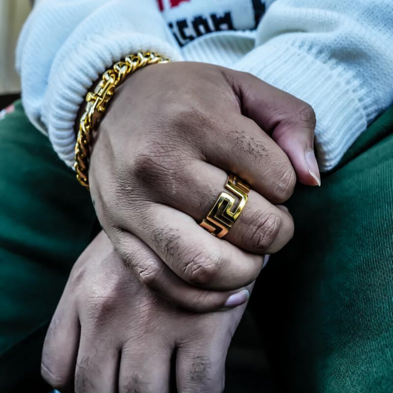 Close-up of a person wearing the greek key ring in gold, with a blurred background.