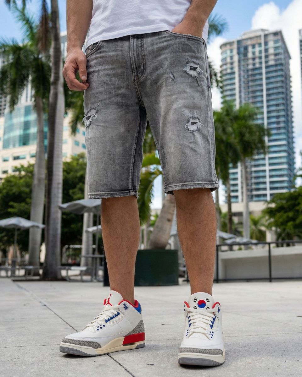 Person wearing gray distressed shorts and white sneakers with colorful accents in an urban setting.