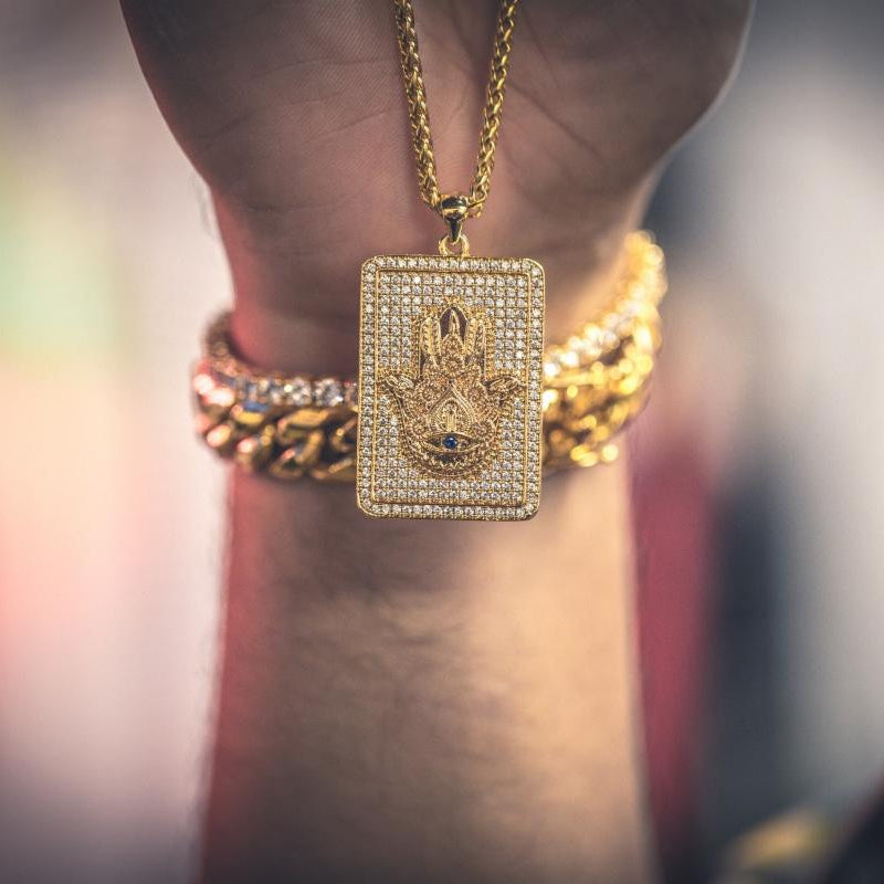 Gold necklace with a rectangular diamond-encrusted hamsa hand pendant on a blurred background