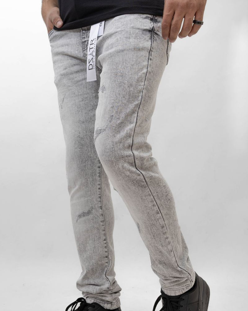 Person wearing gray jeans with a brand logo and black shoes on a white background