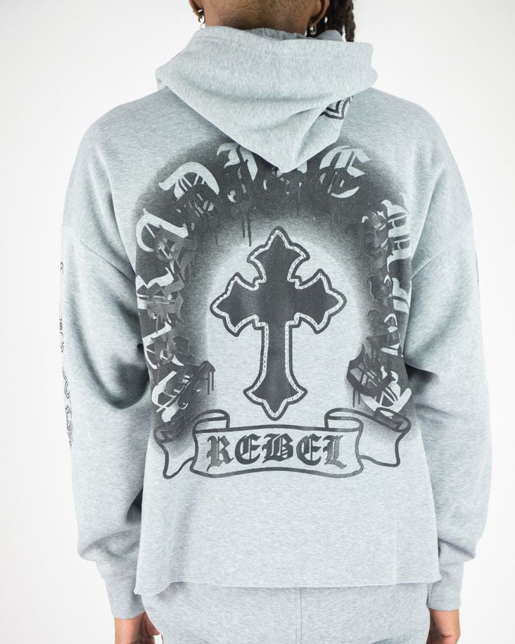 Gray hoodie with a cross and 'REBEL' design on the back, worn by a person.