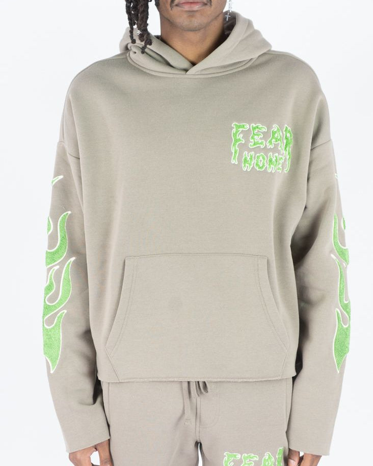 Person wearing a beige hoodie and pants with green text and designs on a white background