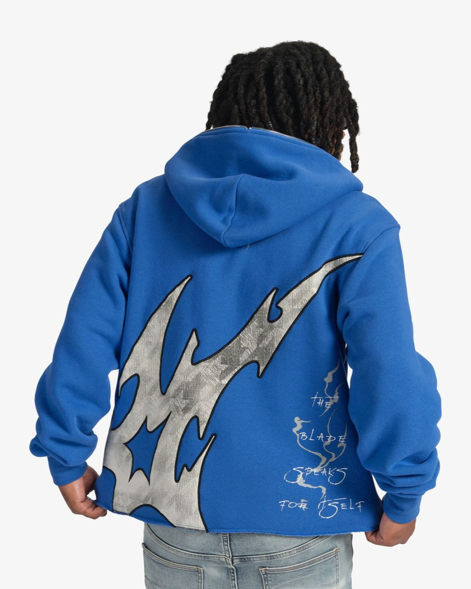 Person wearing a blue hoodie with a large gray flame design on the back, on a white background