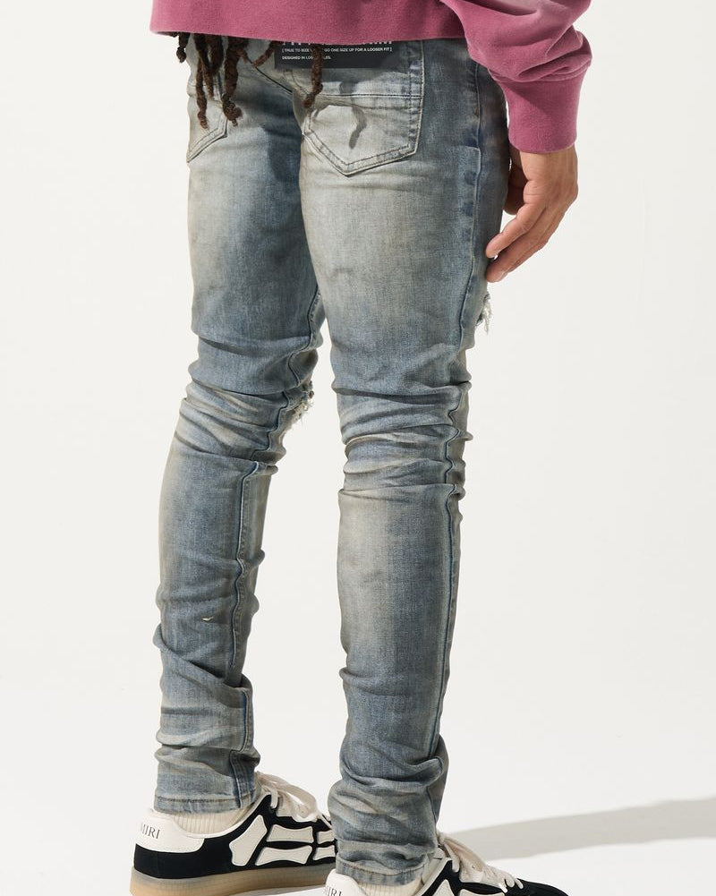 Person wearing light blue distressed jeans and black and white shoes on a plain background