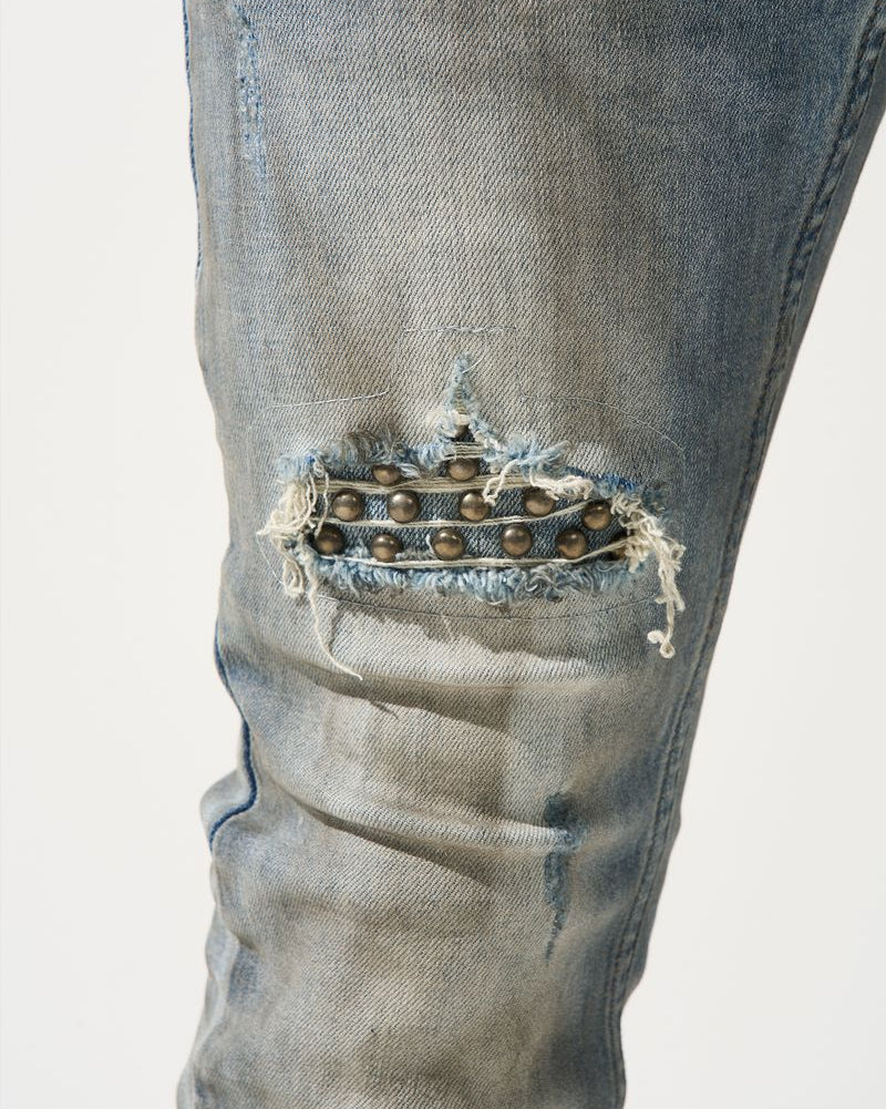 Close-up of distressed denim jeans with a decorative element on a light gray background