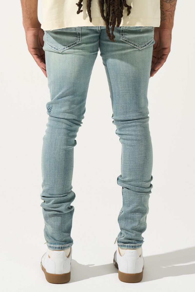 Person wearing light blue jeans and white shoes on a plain background