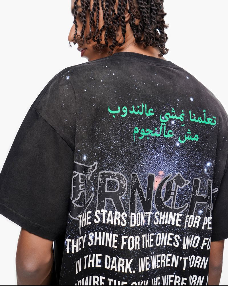 Person wearing a black t-shirt with text and graphics on the back, including Arabic script and a quote.