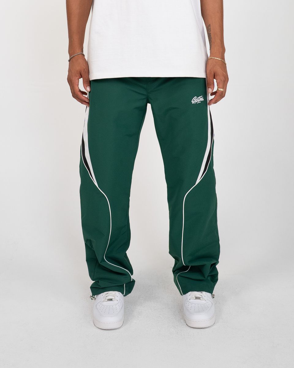 Green track pants with white accents worn by a person on a white background