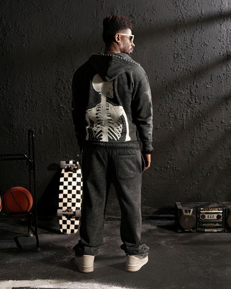 Person wearing a dark hoodie with a skeleton design, standing in a dimly lit room.
