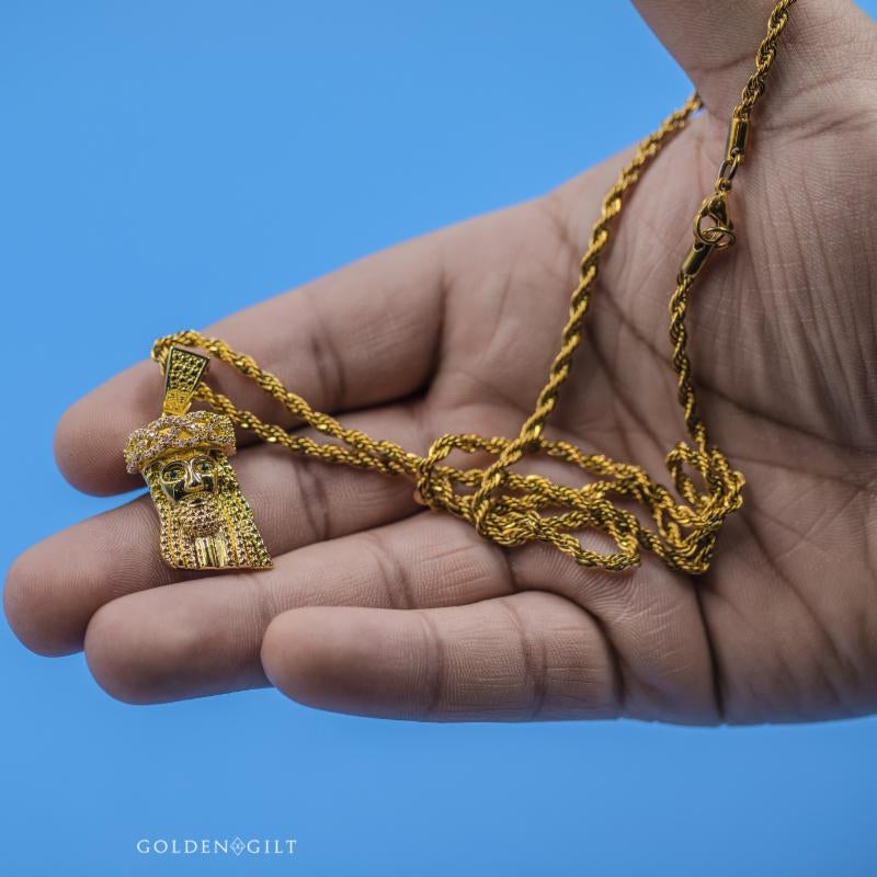 Gold necklace with a mini Jesus pendant held in a hand against a blue background