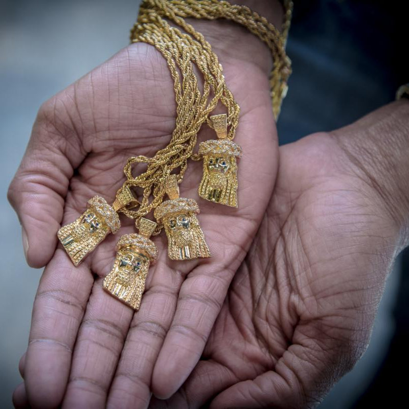 several gold mini Jesus necklaces held in hands with a blurred background