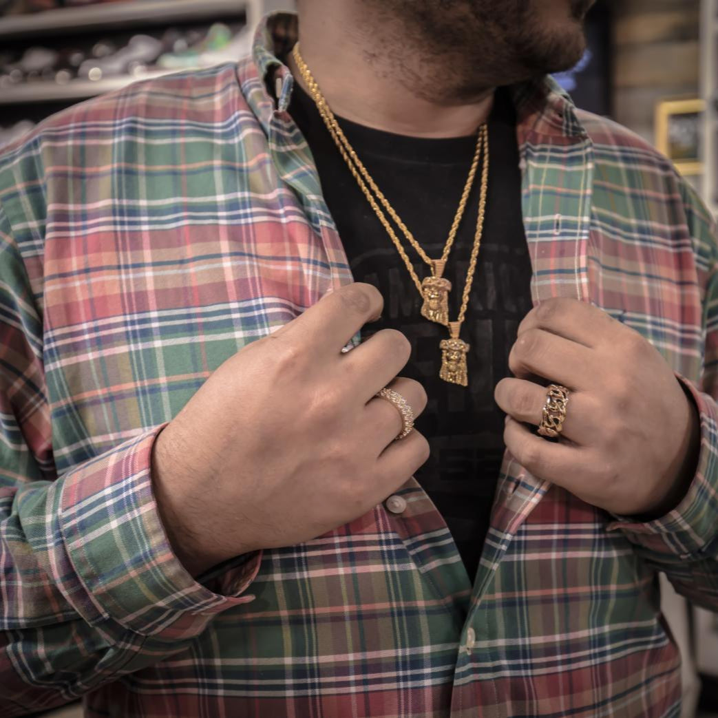 Man wearing a plaid shirt and gold jewelry, including mini Jesus necklaces and rings.