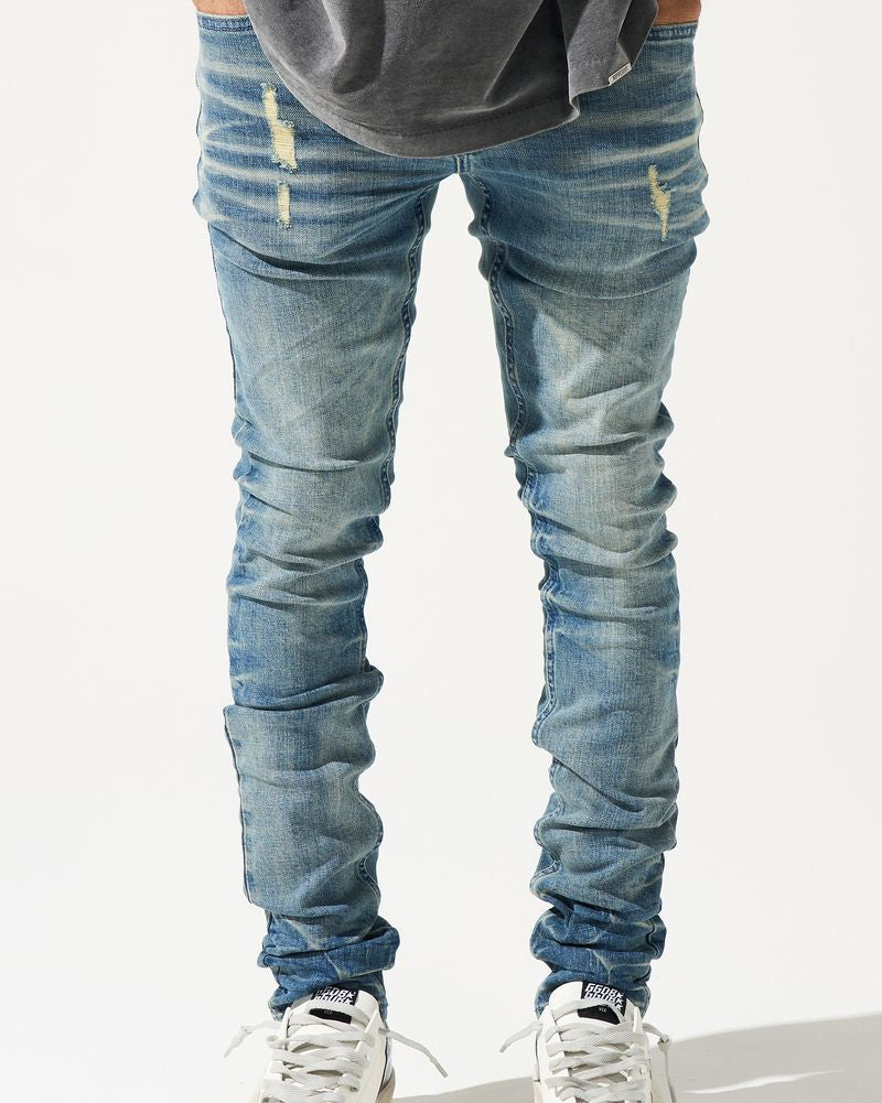 Person wearing distressed blue jeans and white sneakers on a light gray background