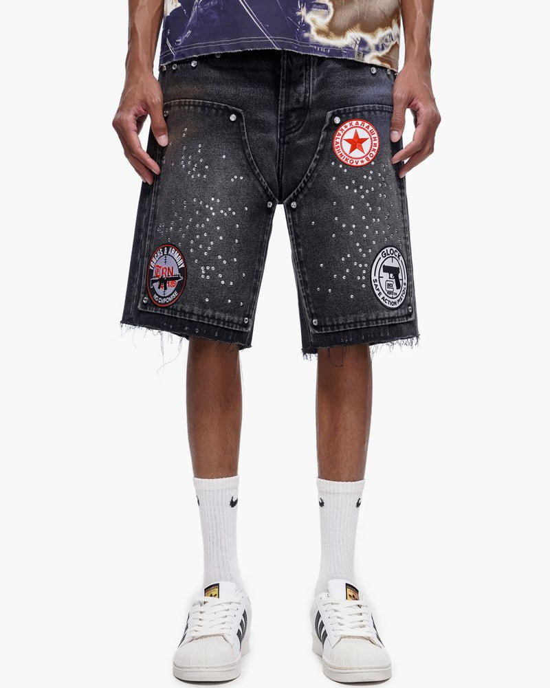 Person wearing black denim shorts with patches on a white background