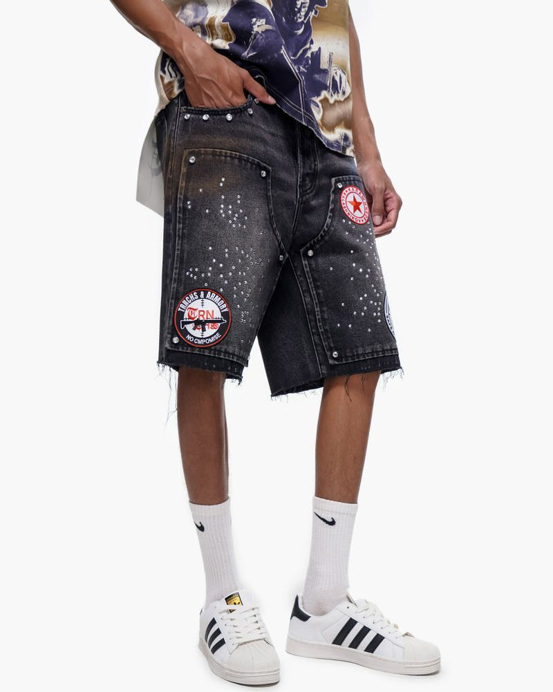 Person wearing black denim shorts with patches and logos, white sneakers, and a colorful shirt.