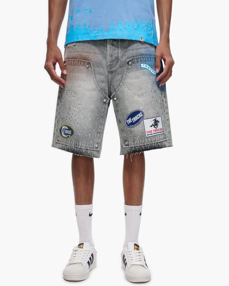 Person wearing gray denim shorts with patches on a white background