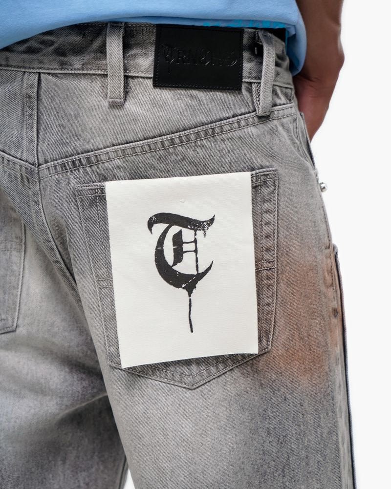 Gray jeans with a white patch featuring a black letter 'T' on a white background